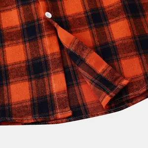 Close-up detail of orange and black plaid shirt showing hem and white button texture