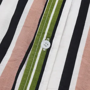 Détail rapproché des rayures verticales colorées et du bouton blanc d'une chemise de plage