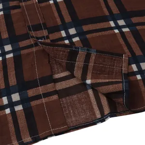 Macro view of brown plaid shirt hem featuring side slit detail and fine stitching