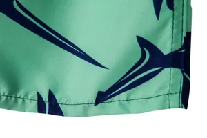Close-up detail showing the navy shark print and fine stitching on green men's beach shorts