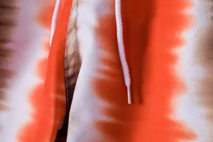 Close-up of vibrant orange tie-dye fabric and white drawstring on men's beach shorts.