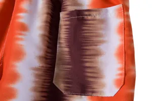Macro detail of the pocket stitching on these orange tie-dye patterned beach shorts.