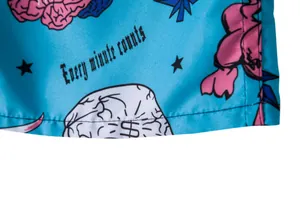 Macro view of blue beach shorts fabric featuring 'Every minute counts' text and brain print