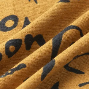 Macro detail of mustard yellow linen fabric featuring black ethnic style print patterns