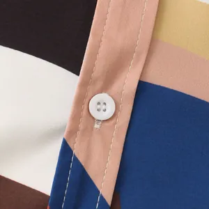 Close-up of white button and stitching on multi-colored patterned men's shirt fabric