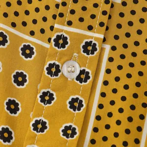 Close-up of yellow shirt fabric with black polka dots, floral prints and white button.