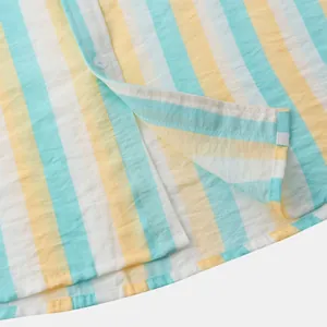 Gros plan détaillé montrant l'ourlet et le bouton d'une chemise de plage rayée jaune et bleu