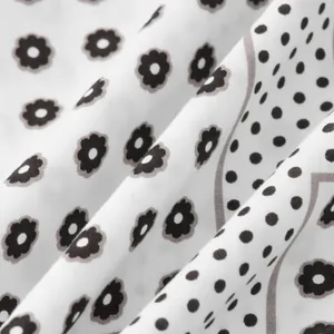 Detailed view of soft white shirt fabric featuring black flower and polka dot patterns.