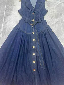 Dettaglio di un abito in denim blu scuro senza maniche con cintura e fibbia dorata.