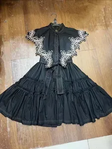 Detailed view of a black A-line dress with white floral embroidery and ruffled skirt layers.