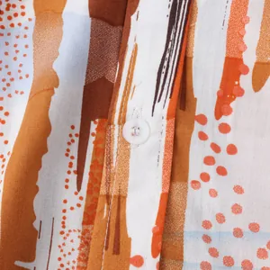 Gros plan d'une chemise de plage pour homme avec imprimé rayé orange et bouton blanc.