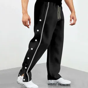 Détail du pantalon de sport noir avec boutons-pression latéraux et une bande grise.