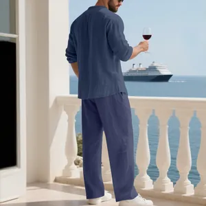 Completo da uomo in lino blu navy su un balcone con vista mare e nave da crociera sullo sfondo.