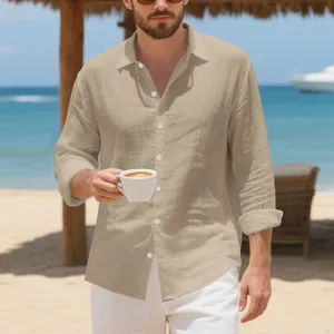 Model in een beige linnen shirt met lange mouwen op een zonnig strand met uitzicht op zee.