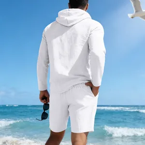 Achteraanzicht van een man in een wit linnen set met hoodie en korte broek op het strand.