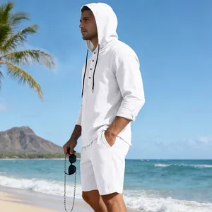 Man in een witte linnen set met hoodie-shirt en korte broek op een tropisch strand
