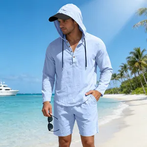 Casual lichtblauw linnen set voor heren met hemd met capuchon en korte broek op een zonnig strand