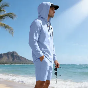 Model draagt een lichtblauw linnen strandset met capuchon op een zonnig tropisch strand