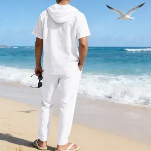 Rückansicht eines weißen Leinen-Set mit Kapuzenhemd und Hose für Herren am Strand
