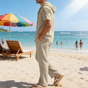Mann am Strand in einem beigen Leinen-Set mit Kapuzenhemd und passender langer Hose im Sommer