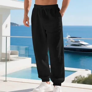 Detailed view of men's black linen joggers with drawstring waist in beach setting