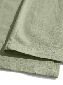 Detailaufnahme des genähten Saums der salbeigrünen Leinenhose für Herren am Strand