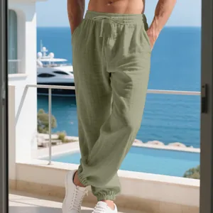Men's olive green linen-cotton joggers on a seaside balcony with elastic cuffs