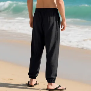 Back view of men's breathable black linen joggers with elasticated cuffs on a sunny beach