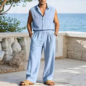 Men's sleeveless linen shirt and long pants resort set in light blue against a seaside backdrop.