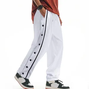 Vue détaillée du pantalon de basket blanc pour homme avec boutons-pression noirs latéraux.