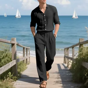 Full body shot of a man in a black linen shirt and pants set walking on a beach boardwalk.