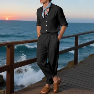 Man in black linen long-sleeve shirt and matching trousers on a sunset beach pier.