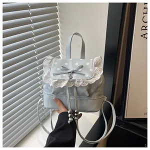 Dettaglio di un mini zaino azzurro con bordo in pizzo bianco e decorazione a fiocco.