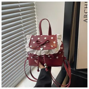 Dettaglio di uno zaino rosso a pois bianchi con pizzo decorativo e fiocco elegante