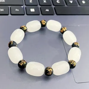 Detailed shot of a white and black beaded bracelet with gold mantra engravings