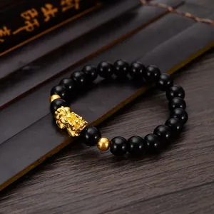 Detailed view of a black obsidian style bracelet with a gold Pixiu charm on a dark wooden desk