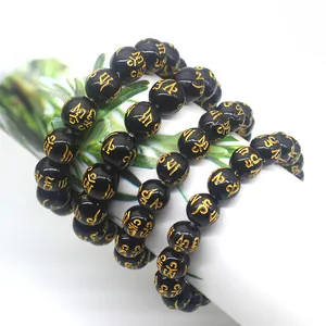 Detailed macro view of black obsidian mantra beads with golden Buddhist engravings.