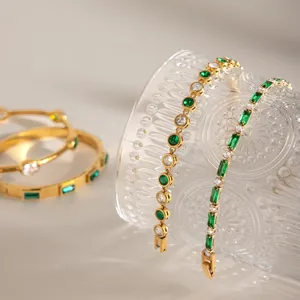 Detalle elegante de pulseras de acero dorado con circonitas esmeralda y blancas