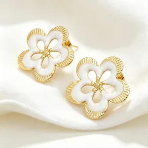 Primer plano de elegantes pendientes de flor dorada con esmalte blanco y bordes texturizados