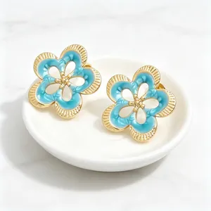 Primer plano de pendientes de flores vintage calados con esmalte azul y acabado oro.