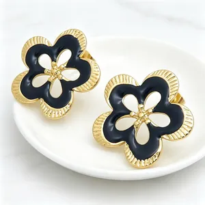 Detalle macro de pendientes de botón de flor retro con esmalte negro y baño de oro