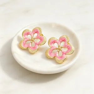 Primer plano detallado de pendientes de flores de esmalte rosa con diseño calado dorado vintage