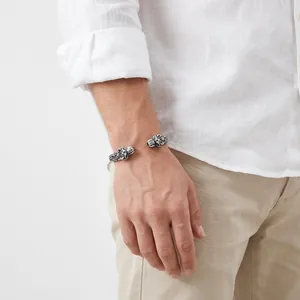Detailed view of a vintage stainless steel double wolf head cuff bracelet on a male wrist.