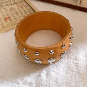 Detaillierte Nahaufnahme eines Vintage Holzarmreifens mit silbernen Metallnieten auf Leinen