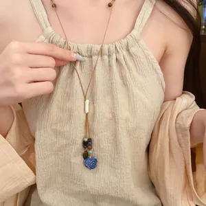 Close-up of leather cord necklace with ceramic blue rose and leaf pendant on model