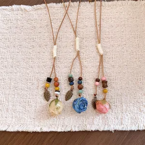 Detail showing handmade resin dried flower pendants with leather cords and leaf charms