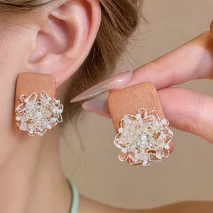 Ethnic style wooden earrings with clear glass flower details, showing ear and hand view.