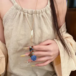 Detail of a handmade necklace with a blue ceramic rose, wooden beads, and a leaf pendant.