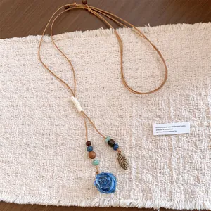 Detailed view of handmade ceramic rose and leaf pendant on adjustable leather cord.