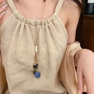 Close-up of bohemian leather cord necklace with blue rose ceramic flower pendant on model